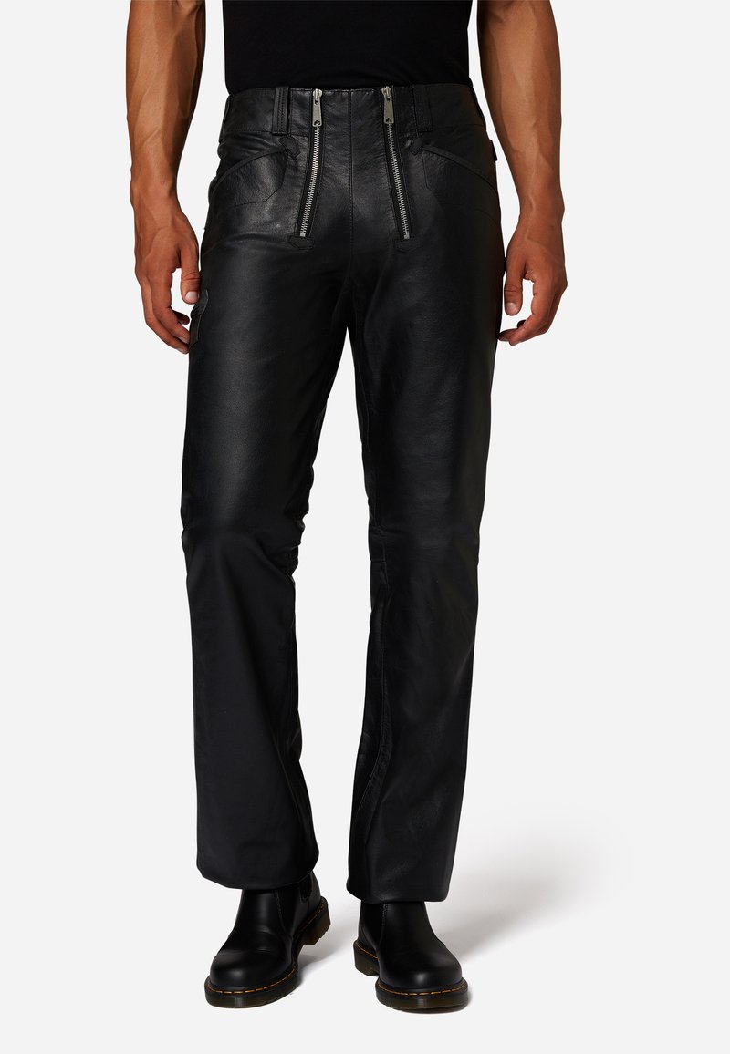 Zwarte leren broek met een rechte snit, twee stevige voorzakken met rits en een gladde textuur, gecombineerd met zwarte laarzen.