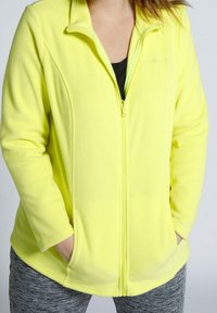 Fluorescency żółta bluza polarowa z zamkiem z przodu, bocznymi kieszeniami i stójką. Materiał ma miękki, teksturowany wygląd.