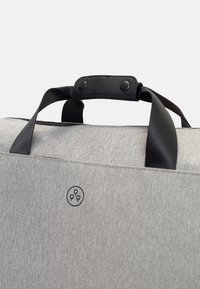 Grå tygväska med svarta läderdetaljer, utrustad med korta handtag, tryckknappar och en logotyp med tre cirklar i en grafisk design.