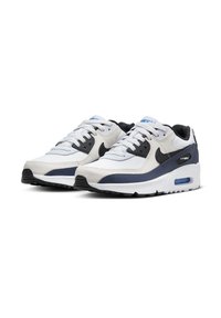 Bílé a námořnické atletické tenisky s vícevrstvým materiálem z mřížky a kůže, s černým logem Nike swoosh, modrými akcenty a viditelnou vzduchovou tlumicí jednotkou.