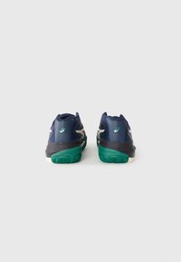Chaussures de sport navy avec une tige synthétique texturée, semelle en caoutchouc verte et accents argentés, dotées d'un talon arrondi et d'un col rembourré.