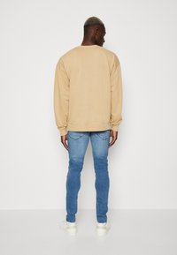 Beige crewneck sweatshirt met geribde manchetten, gecombineerd met lichtblauwe slim-fit jeans en witte sneakers, gezien vanuit de achterkant.