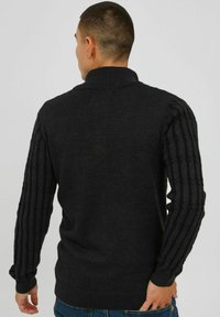 Navy sweater with a high collar and textured ribbed sleeves. Made of knit fabric, featuring a solid body and contrasting sleeve pattern.