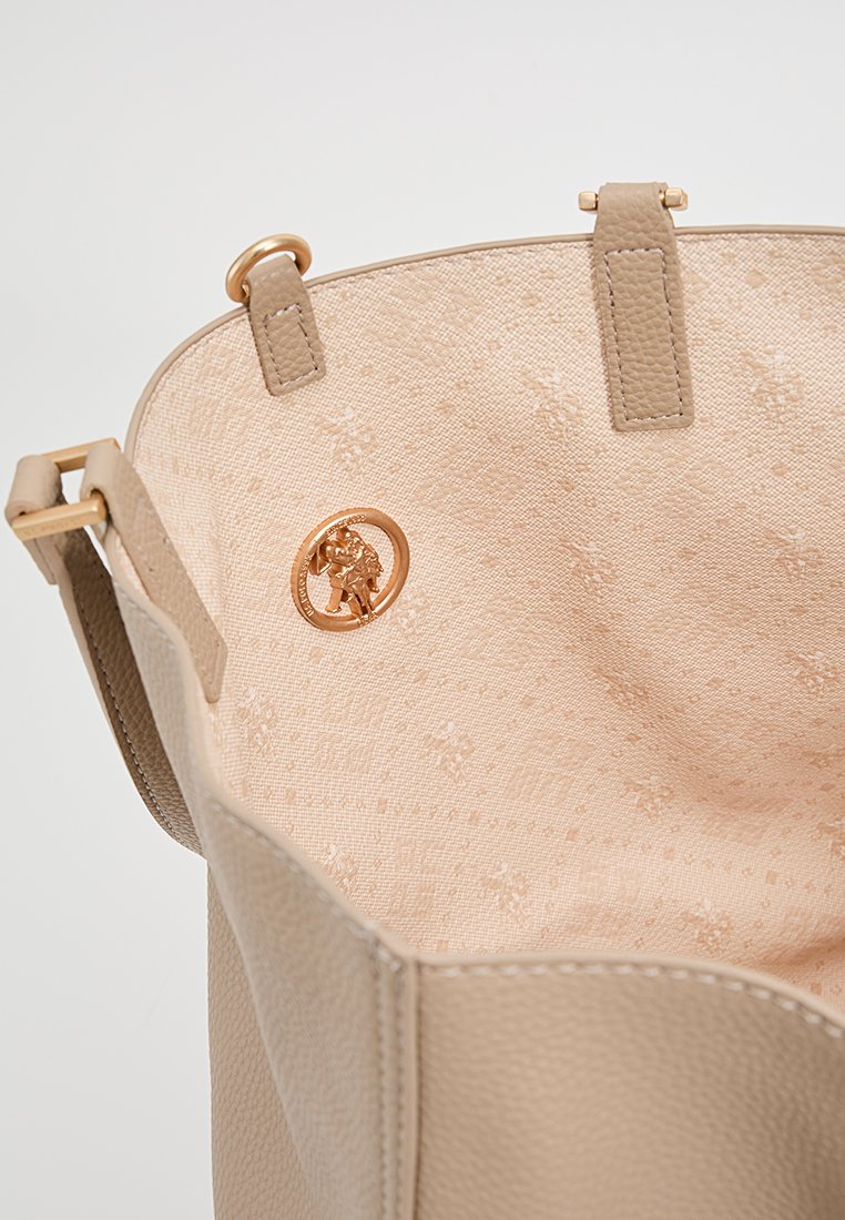 Sac à main en cuir beige avec un intérieur texturé, mettant en avant un accent logo doré et de subtils motifs floraux sur la doublure.