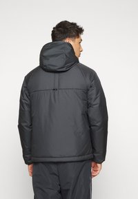 Black puffer jacket with a hood, featuring a smooth texture, elastic cuffs, and a simple design. Back view shows a seam across the upper back.