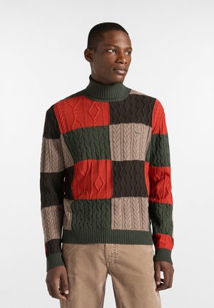 Suéter multicolorido con un diseño de patchwork y texturas de punto de cable en rojo, verde, marrón y beige. Cuello acanalado alto.