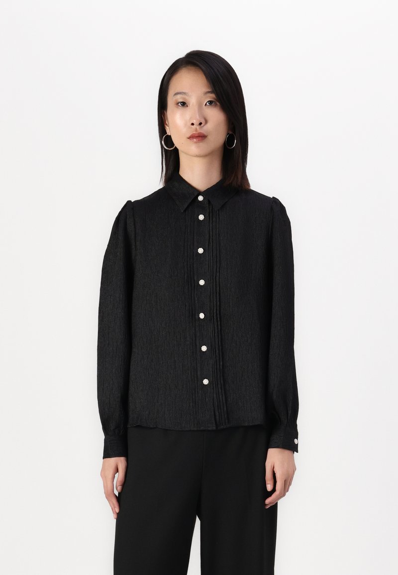 Black long-sleeve blouse with a collared neckline, pleated texture, and button closure featuring decorative pearl-like buttons.