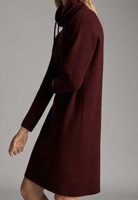 Burgundy neuletunika, jossa on korkea kaulus, pitkät hihat ja rento istuvuus, jossa on ribbitekstuurilla varustetut hihansuut ja helma.