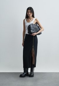 Μαύρη midi φούστα με φερμουάρ στο πλάι, σε συνδυασμό με ένα άσπρο tank top και μαύρες δερμάτινες μπότες. Το μοντέλο κρατά μια δομημένη μαύρη τσάντα.