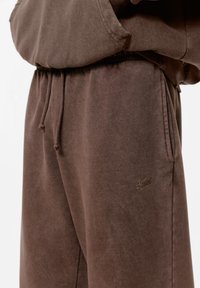 Bruine katoenen sweatpants met een zachte textuur, voorzien van een elastische tailleband en een trekkoord, en een subtiele geborduurde logo op het been.