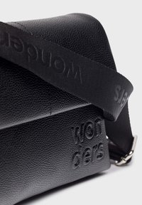 Czarna torebka crossbody z fakturowanej skóry, z wytłoczonym logo "Sandqvist" oraz dopasowanym czarnym regulowanym paskiem na ramię z subtelnym brandingiem.