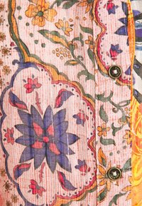 Tissu à motif floral avec de grandes fleurs violettes et orange, des vignes vertes, et deux boutons métalliques gravés.