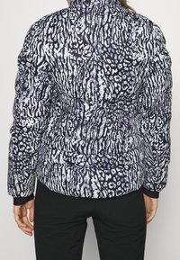 Doudoune avec un motif abstrait noir et blanc, dotée d'un col montant, d'une texture matelassée et de poignets élastiques.