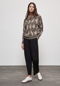 Sweatshirt vert à motif géométrique avec des manches longues, associé à un pantalon noir ample et des chaussures de sport blanches.
