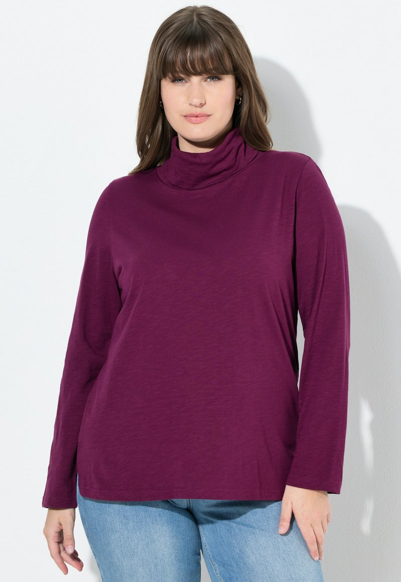 Langsleeve turtlenecktop in diep paars, gemaakt van zachte stof met een ontspannen pasvorm en zijsplitten, gecombineerd met lichtblauwe spijkerbroek.