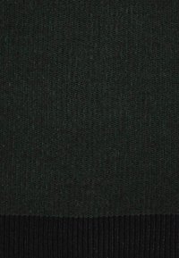 Mörkgrön stickad tyg med en strukturerad mönster, övergår till en solid svart ribbad fåll i botten.