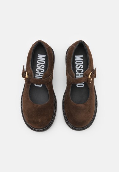 Pantofi Mary Jane din suede maro, cu vârf rotund, curea ajustabilă și cataramă de culoare aurie. Interiorul dispune de o talpă cu logo negru.