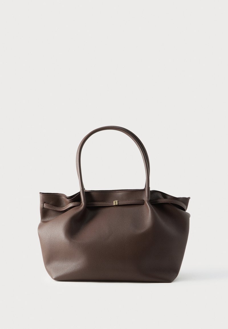 Καφέ δερμάτινη τσάντα ώμου με δύο επιμήκη χερούλια, με υφή και διακριτική μεταλλική λεπτομέρεια μπροστά.