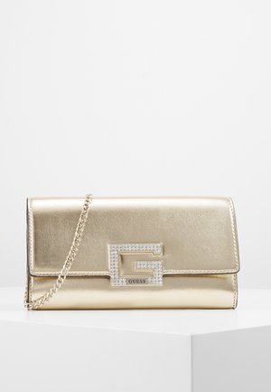 Bolso clutch metálico dorado con una correa de cadena, que presenta un gran logo "G" adornado con piedras de imitación y la marca GUESS en la solapa frontal.