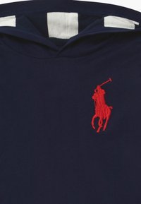 Sweat à capuche bleu marine avec un logo de cheval brodé en rouge sur la poitrine, doté d'une capuche à cordon de serrage et d'une doublure rayée blanche contrastante.