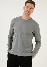 Szürke bordázott, hosszú ujjú póló kerek nyakkal és egy kis V-varrással a nyakrésszel. Puha textúra, testhezálló fazon.