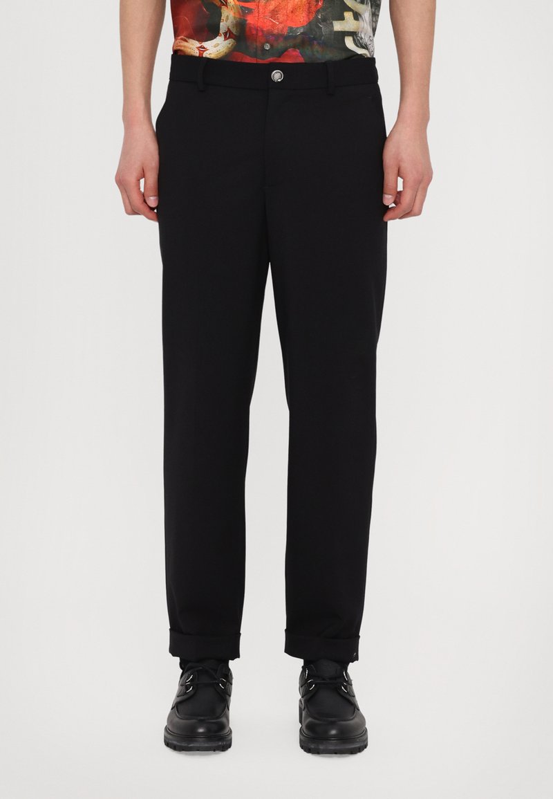 Μαύρα παντελόνια με ίσια γραμμή, που διαθέτουν κουμπί κα�ι γυρισμένα μανίκια. Φορεμένα με μαύρα παπούτσια και έναχρωματιστό μοτίβο μπλουζάκι.