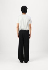 T-shirt gris à manches courtes et pantalon large noir vus de dos. Le pantalon présente deux poches arrière et une coupe droite.