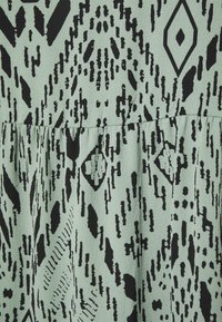 Kangasta mint vihreä, jossa on mustia geometristen tribaalikuosiset kuvioita ja kerätty sauma keskellä.