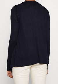 Cardigan lungo blu navy con una vestibilità comoda, texture a coste e scollatura rotonda, indossato sopra pantaloni chiari.