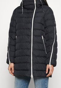 Czarna kurtka puchowa z kapturem, z poziomym pikowaniem, białymi suwakami, bocznymi kieszeniami oraz regulowanymi sznurkami w kapturze.