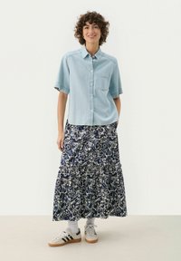 Light blue short-sleeve button-up shirt with a chest pocket, paired with a navy floral-patterned tiered skirt and white sneakers.