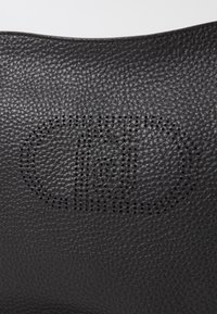 Pelle nera texturizzata con un design di logo circolare perforato. Il materiale appare morbido, mostrando schemi e profondità distinti.