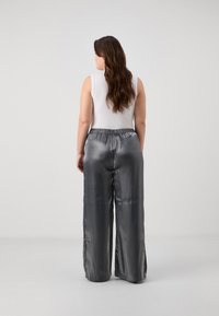 Silver satin wide-leg pants with an elastic waistband and side slits, paired with a fitted white sleeveless top, viewed from the back.