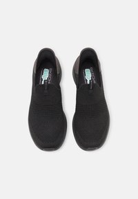 Black slip-on sneakers with a textured upper and smooth accent detailing. Features a cushioned sole and elastic band for easy wear.