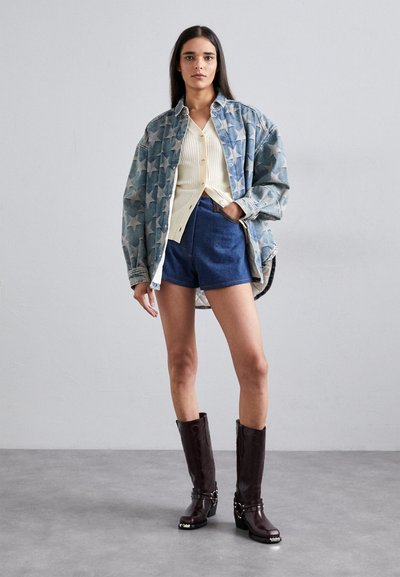 Denim jakna s sivim vzorcem zvezd, smetanasta rebrasta kardigan, modri šorti in rjave škornje do kolen s srebrnimi detajli. Teksturne obdelave.