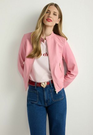 Różowa kurtka bomberka z imitacji skóry, z okrągłym kołnierzem i kieszeniami na zamek, w połączeniu z białym t-shirtem i niebieskimi dżinsami z wysokim stanem.