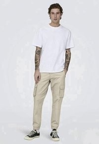White cotton t-shirt, relaxed fit, paired with beige cargo pants featuring side pockets, complemented by black and white sneakers.