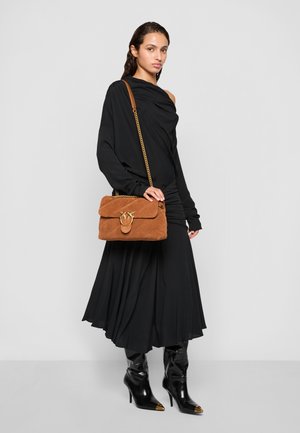 Brown suede handbag with a flap, gold hardware detail, paired with a black draped dress and knee-high black heeled boots, standing on a plain background.
