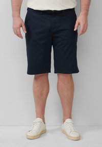 Marineblaue Shorts aus leichtem Material, mit geradem Schnitt und flachem Bund, kombiniert mit weißen Sneakers mit Gummisohlen.