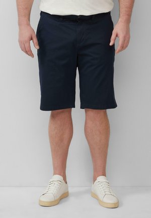 Marineblauwe shorts van lichtgewicht stof, met een rechte snit en een platte voorkant, gecombineerd met witte sneakers met een gumrubberen zool.