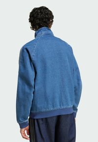 Jeansjacka i medelblått med hög krage, ribbade ärmslut och midja, med en avslappnad passform och raglanärmar, strukturerad yta.