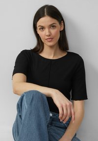 Zwarte geribbelde top met korte mouwen en een ronde halslijn, gecombineerd met lichtblauwe denim jeans. De stof heeft een gestructureerd patroon.