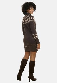 Abito in maglia marrone scuro fino al ginocchio, caratterizzato da una yoke chiara e decorata e maniche lunghe. Indossato con stivali alti marrone scuro.