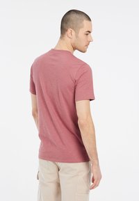 Tričko s krátkym rukávom a okrúhlym výstrihom v tlmenej ružovej farbe, vyrobené z mäkkej bavlny, s voľným strihom a hladkým povrchom.