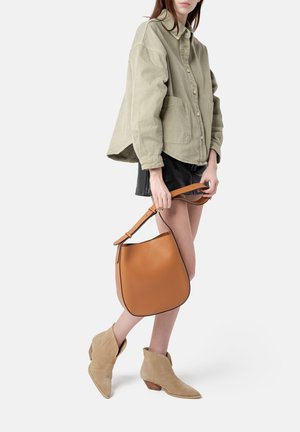 Tan leather bucket bag with a contrasting trim, paired with a light olive green oversized jacket, black shorts, and beige suede ankle boots.