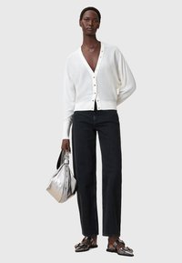 Valkoinen villasekoite kardigan, jossa on V-pääntie ja nappilukko, yhdistettynä mustiin suoralahkeisiin farkkuihin ja metallinhohtoiseen hopeiseen käsilaukkuun. Hermès-tyyliset sandaalit.