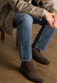 Bruine suède enkellaarzen met een ronde neus, vetersluiting en minimale hardware, gecombineerd met lichtblauwe rechte jeans.