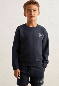 Dunkelblaues Sweatshirt und passende Shorts aus weichem Material. Das Sweatshirt hat einen Rundhalsausschnitt und ein Logodetail auf der Brust.