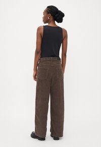 Bruine corduroy wijde broek met een gestructureerde afwerking en twee achterzakken, gecombineerd met een zwart mouwloos topje en zwarte chunky laarzen.