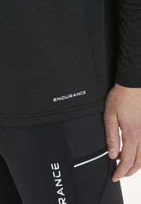 Sort atletisk skjorte med "ENDURANCE" logo i hvid, parret med sorte leggings med hvide accenter og strukturerede syninger.